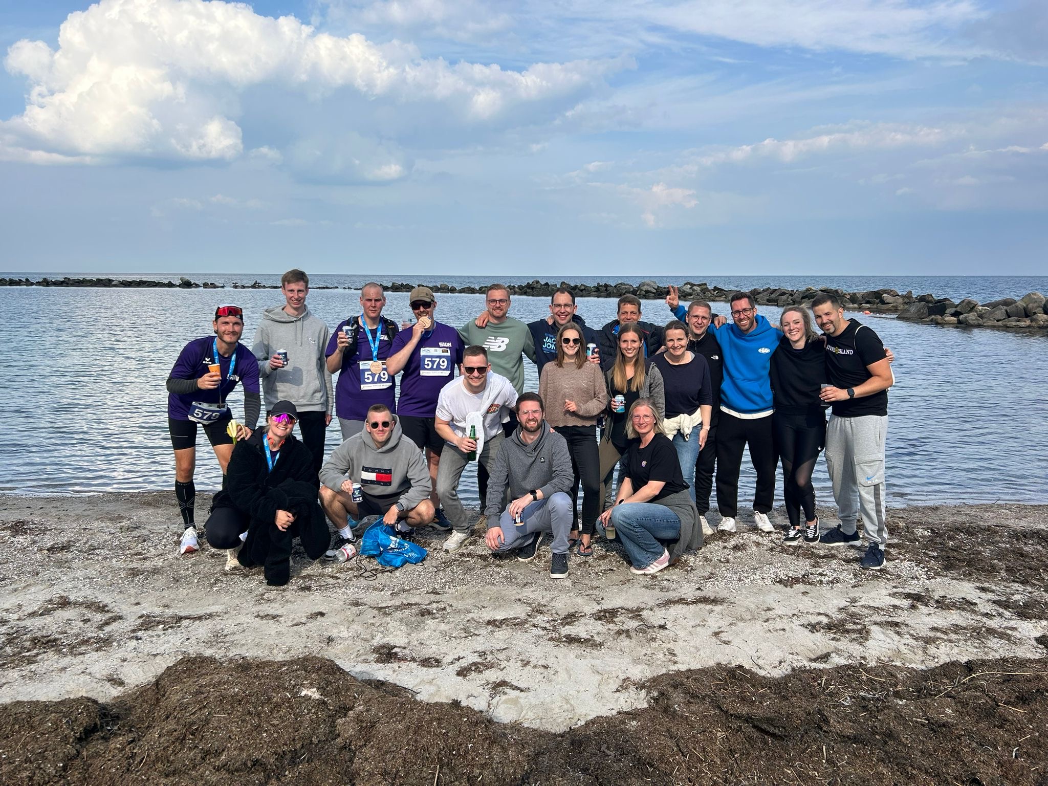 Eine große Gruppe von Sportlerinnen und Sportlern feiert am Strand nach einem Lauf, einige tragen Medaillen um den Hals.