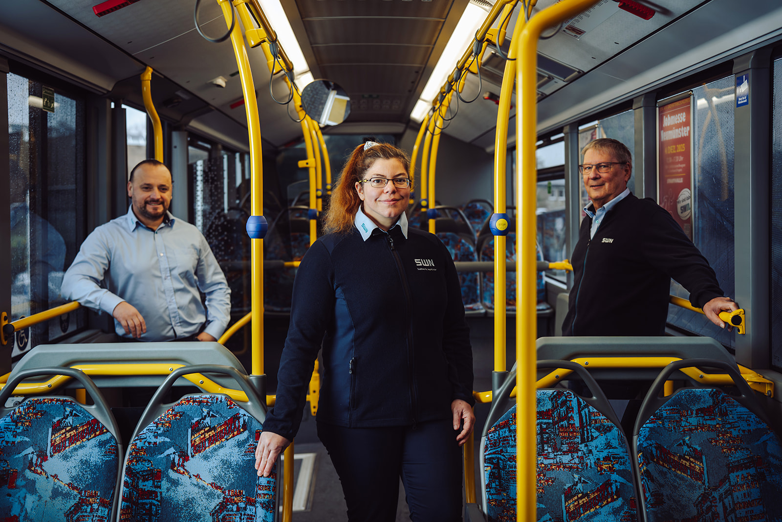 Drei Mitarbeiter von SWN stehen lachend nebeneinander vor einem Fahrzeug des Mobilitätsservices Hin & Wech. Das Fahrzeug trägt das typische SWN-Design und ist im Hintergrund sichtbar, während die Mitarbeiter ihre Arbeitsjacken mit dem SWN-Logo tragen.